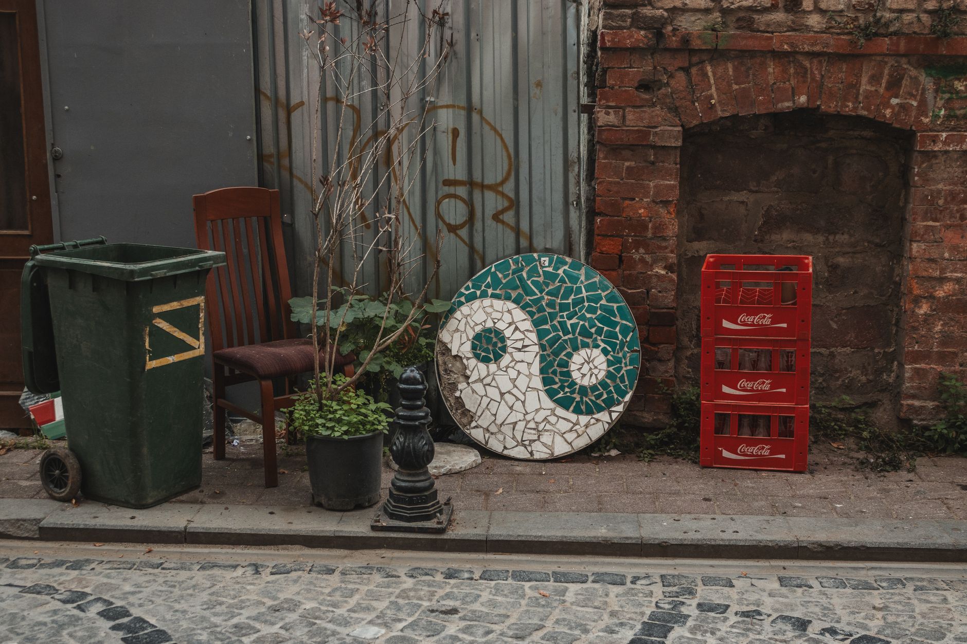 Rustic urban alley with yin-yang mosaic, Coca-Cola crates, and potted plants.
