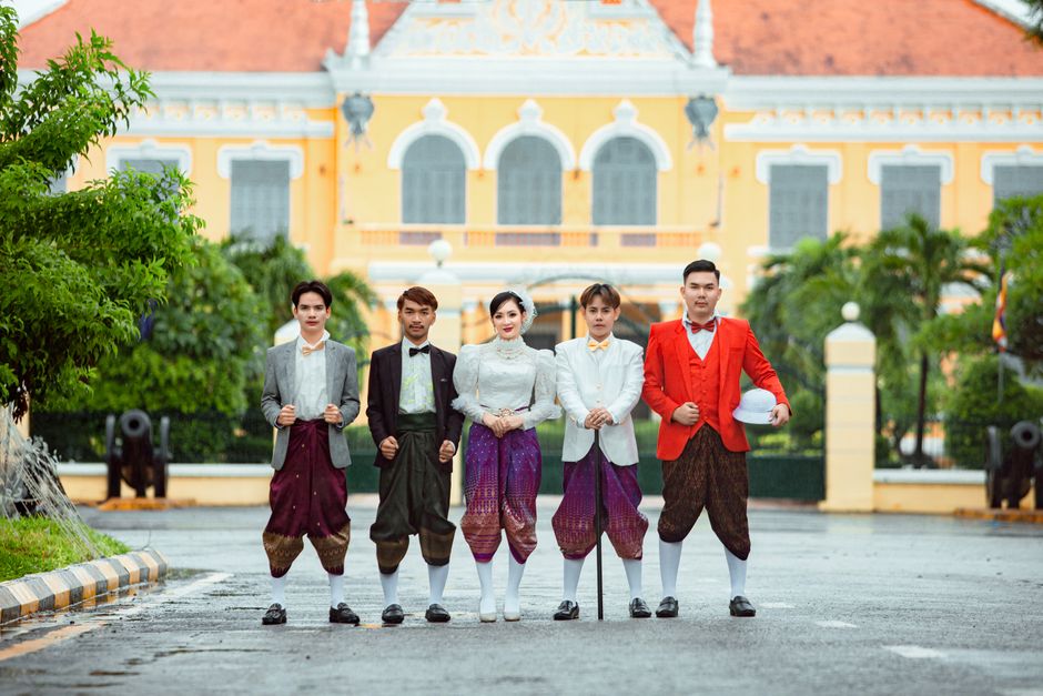 A group of young people in traditional Khmer clothing posing in front of a historic building.