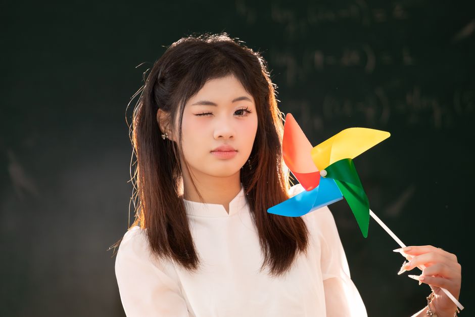 Young girl winking holding a vibrant pinwheel, symbolizing playfulness and joy.