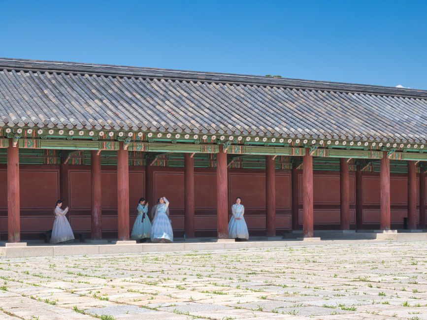 Women in traditional Korean hanbok stand by a historical palace in Seoul, showcasing cultural heritage.