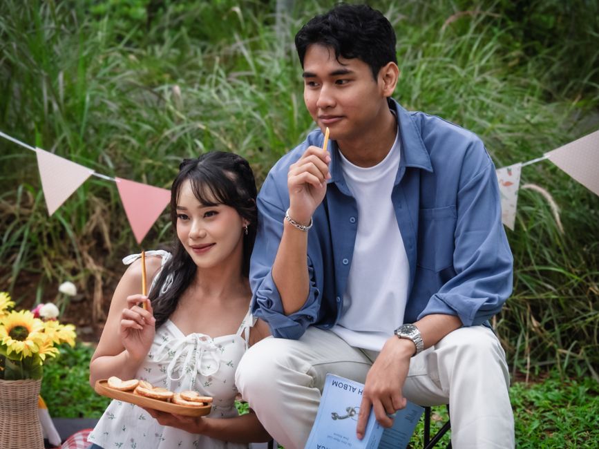 A cheerful young couple enjoying a picnic outdoors with snacks and books in Jakarta, Indonesia.