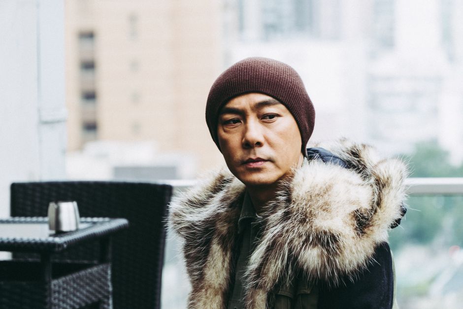 Outdoor portrait of an east Asian man wearing a beanie and fur-trimmed coat.