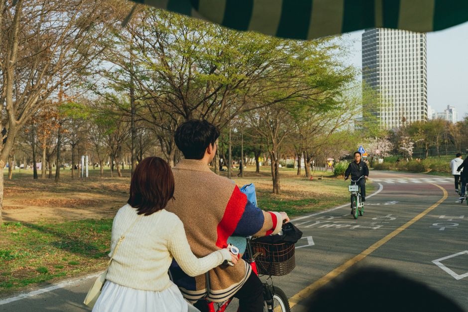 Couple cycling in a vibrant Seoul park during springtime, enjoying nature.