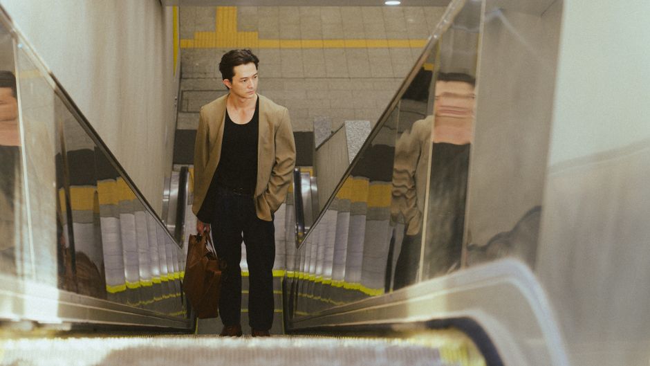 A young man in a modern outfit riding an escalator in a subway station.