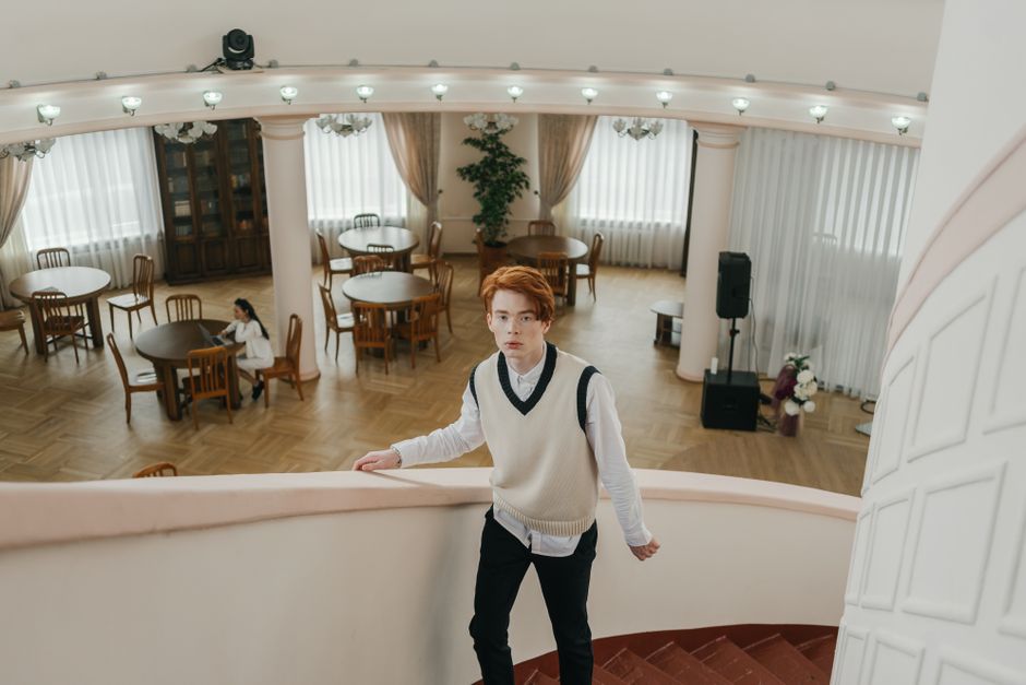Young man in elegant vest standing on a staircase inside a spacious room.