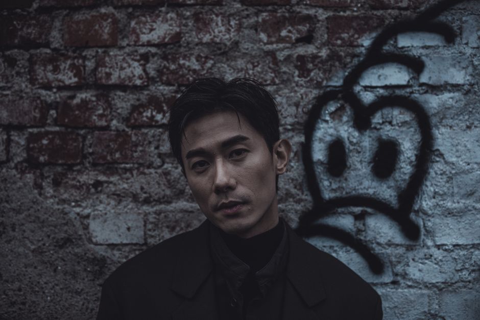 Dark and dramatic portrait of a man in front of a graffiti brick wall.