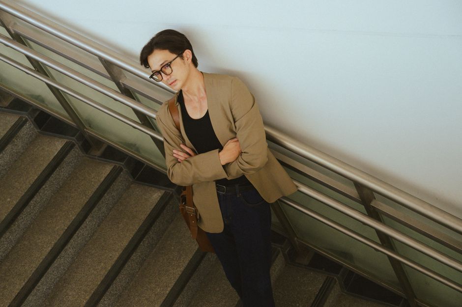 Young adult in casual attire leaning on a staircase railing indoors.