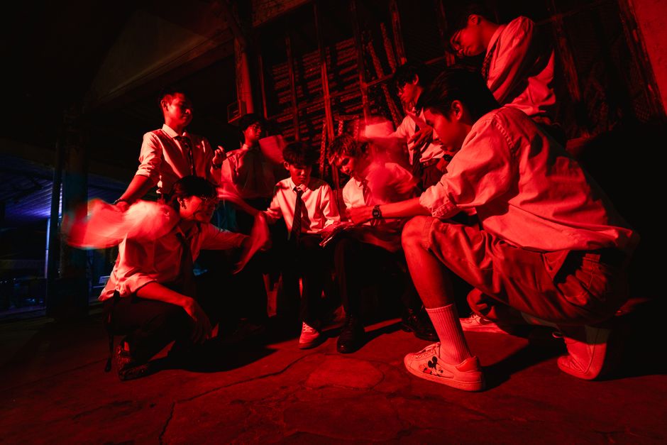 Group of men planning in a dimly lit urban setting with red lighting.