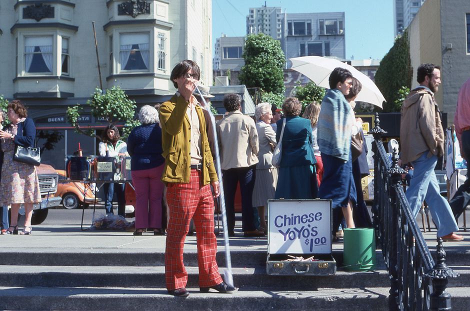 Vibrant city street with people gathered around a street vendor selling Chinese yo-yos.