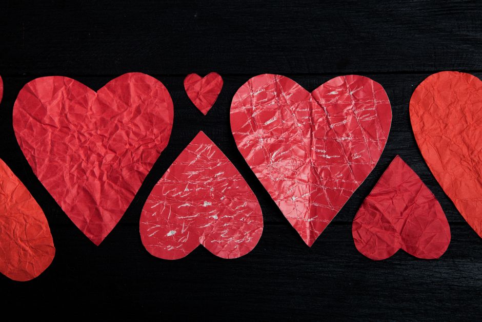 Crumpled red paper hearts arranged on a black backdrop symbolizing love and romance.