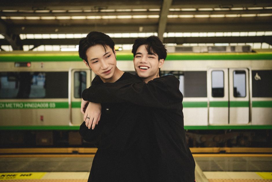 Two young men embracing and smiling on a train platform, exuding friendship and joy.