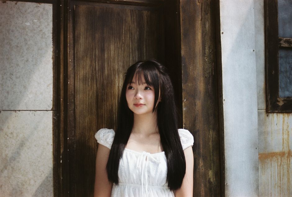 Young woman in a white dress stands by a rustic wooden door, creating a serene and classic portrait.